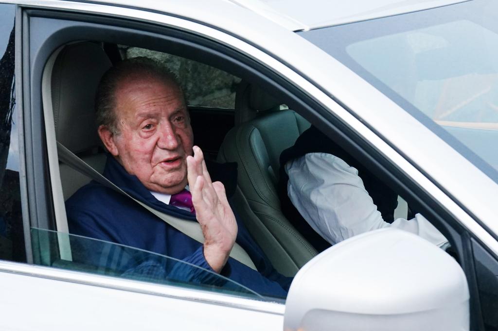 King Juan Carlos waves from the passenger seat of a car.