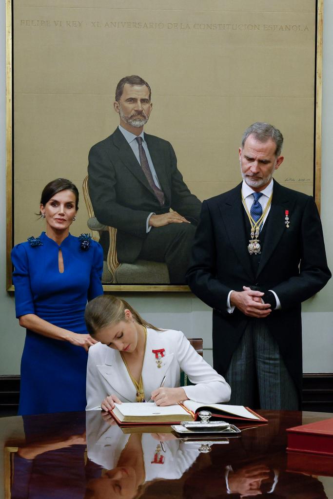 Princess Leonor signing a book with her parents behind her